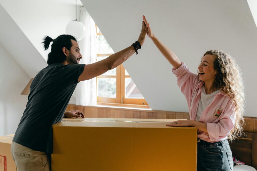 pexels photo 4246061 4246061 Young couple high-fiving in their new home, happily surrounded by moving boxes.